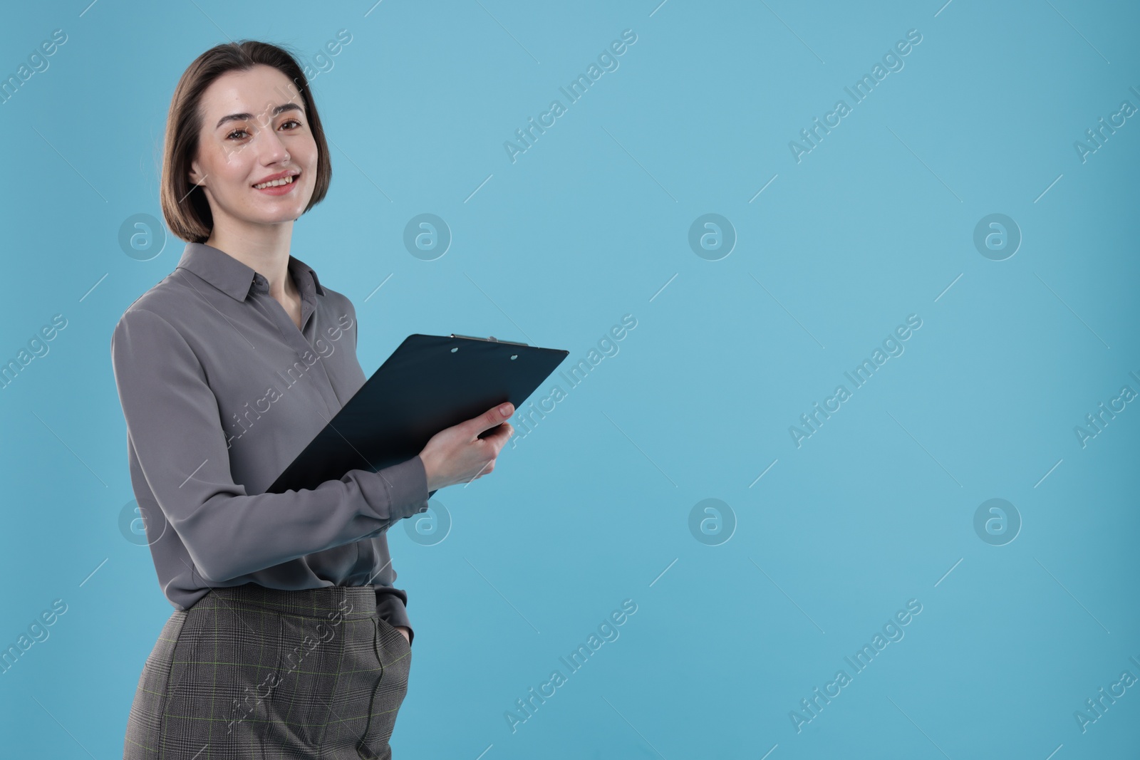 Photo of Portrait of smiling secretary with clipboard on light blue background. Space for text