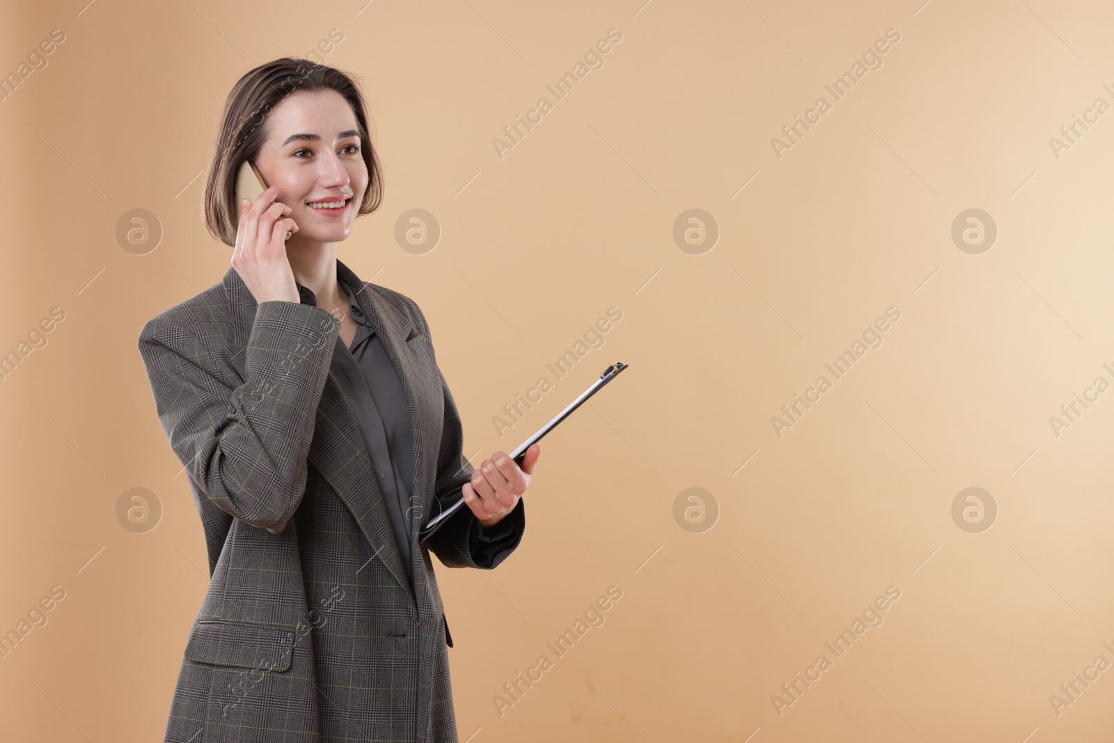 Photo of Smiling secretary with clipboard talking on smartphone against dark beige background. Space for text