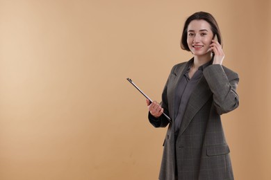 Photo of Smiling secretary with clipboard talking on smartphone against dark beige background. Space for text