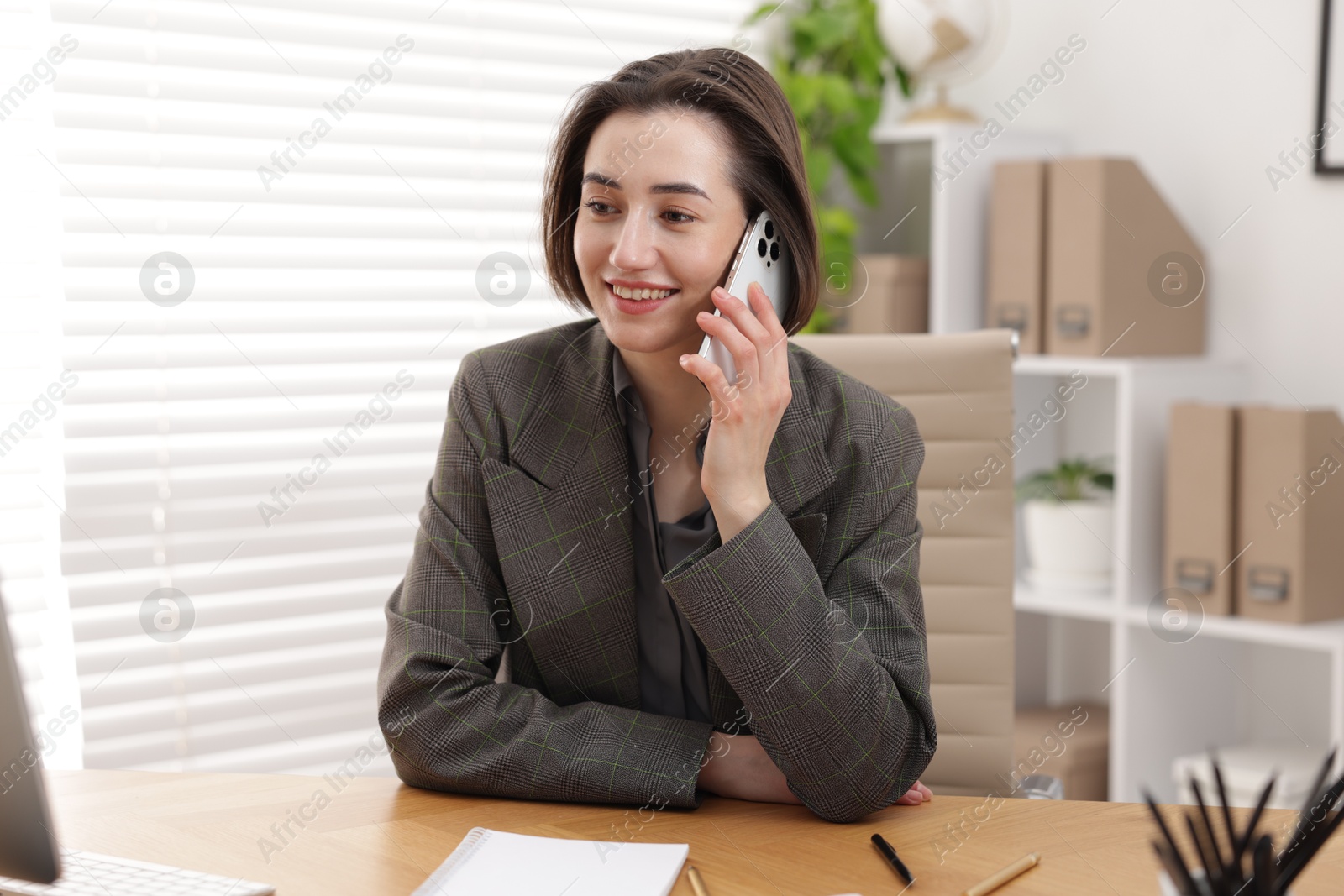 Photo of Secretary talking on smartphone while working at table in office