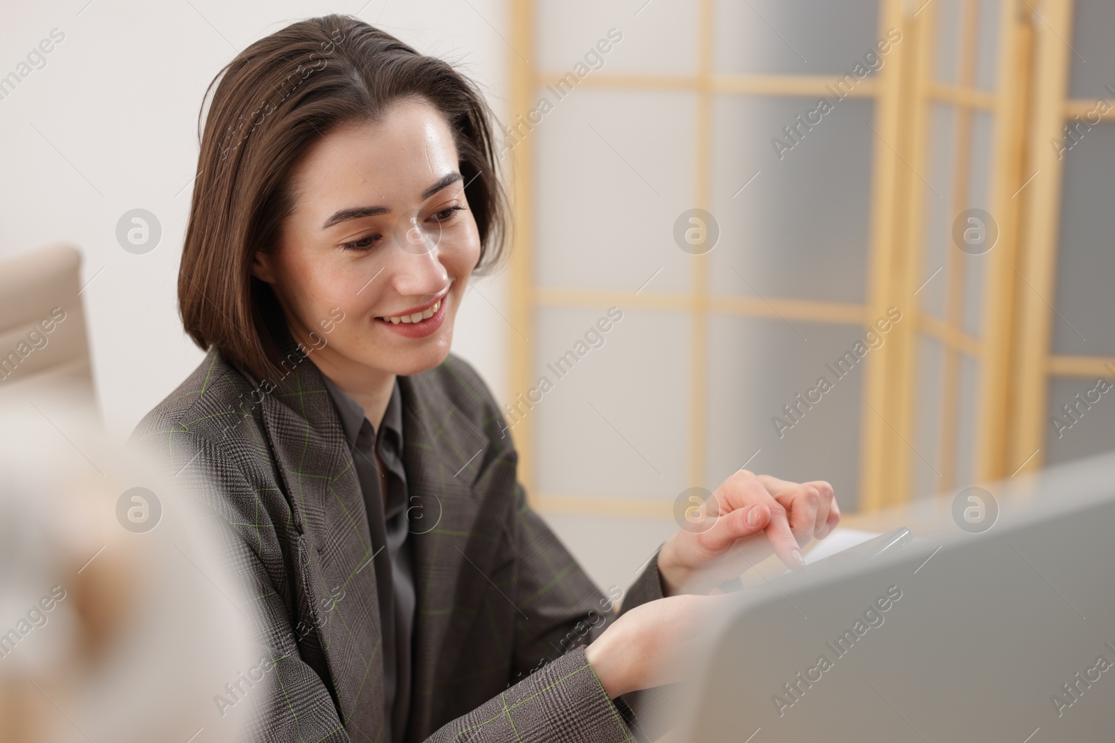 Photo of Smiling secretary with smartphone working on computer in office