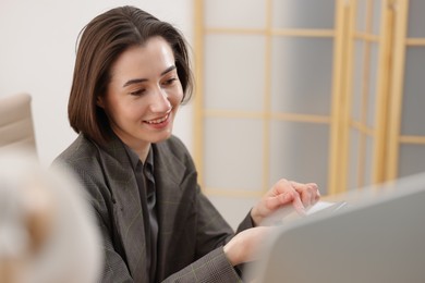 Photo of Smiling secretary with smartphone working on computer in office