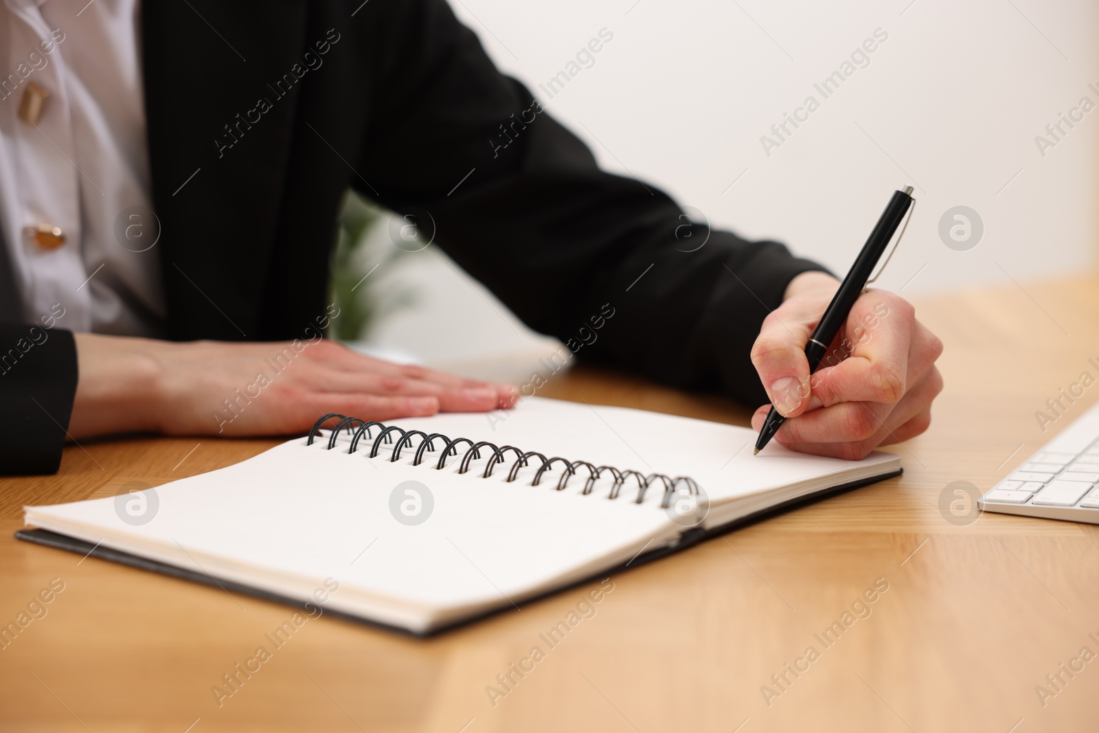 Photo of Secretary taking notes at wooden table indoors, closeup