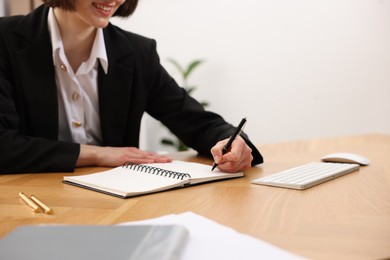 Photo of Secretary taking notes at wooden table indoors, closeup. Space for text