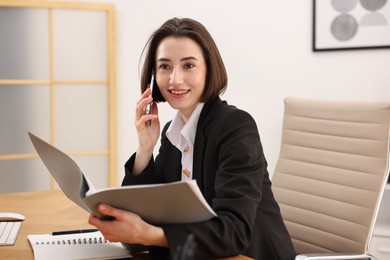 Photo of Secretary talking on smartphone while working with documents at table in office