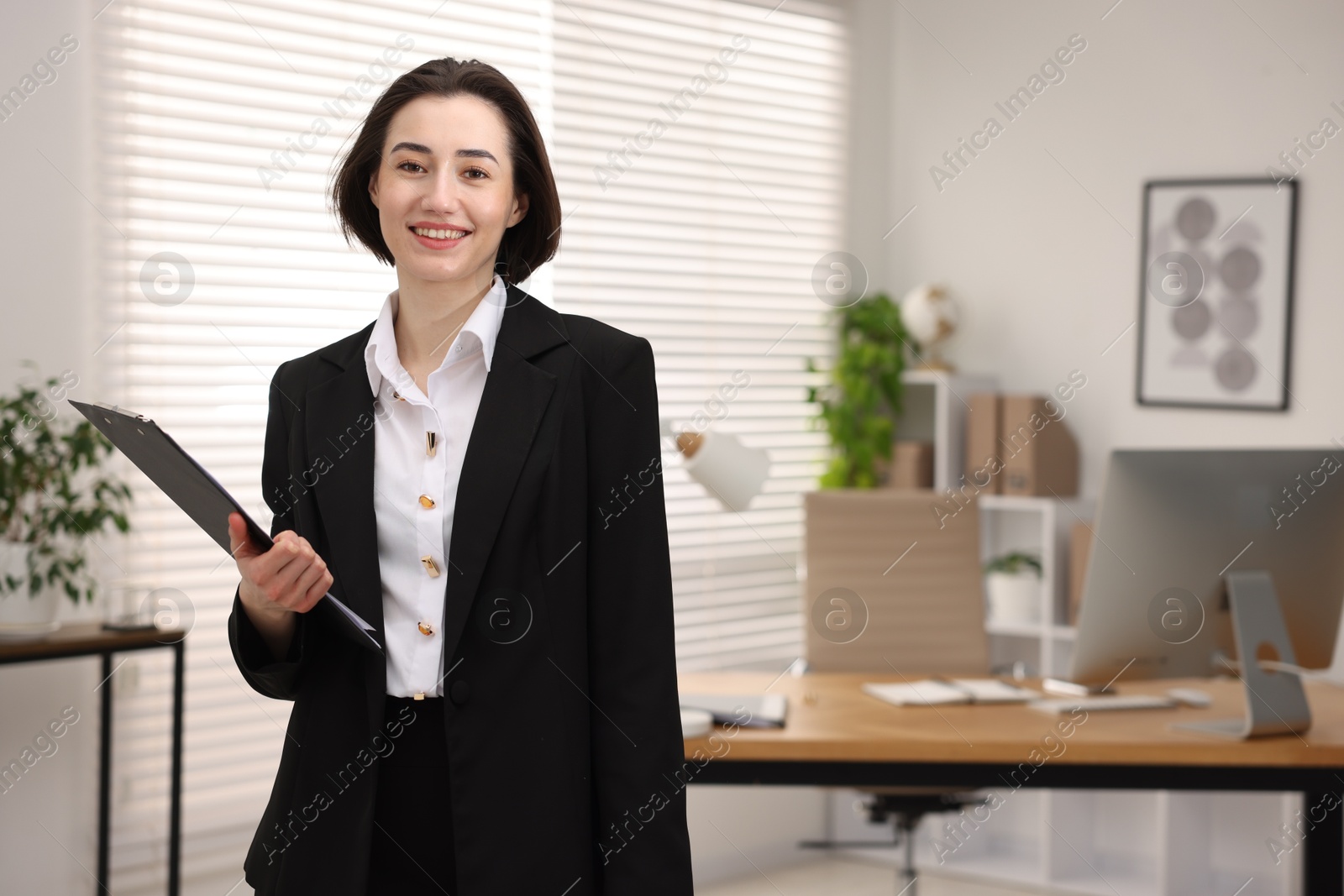 Photo of Portrait of smiling secretary with clipboard in office. Space for text