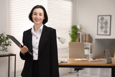 Photo of Portrait of smiling secretary with clipboard in office. Space for text