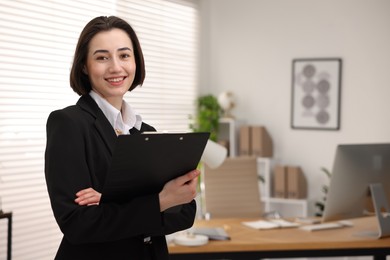 Photo of Portrait of smiling secretary with clipboard in office. Space for text