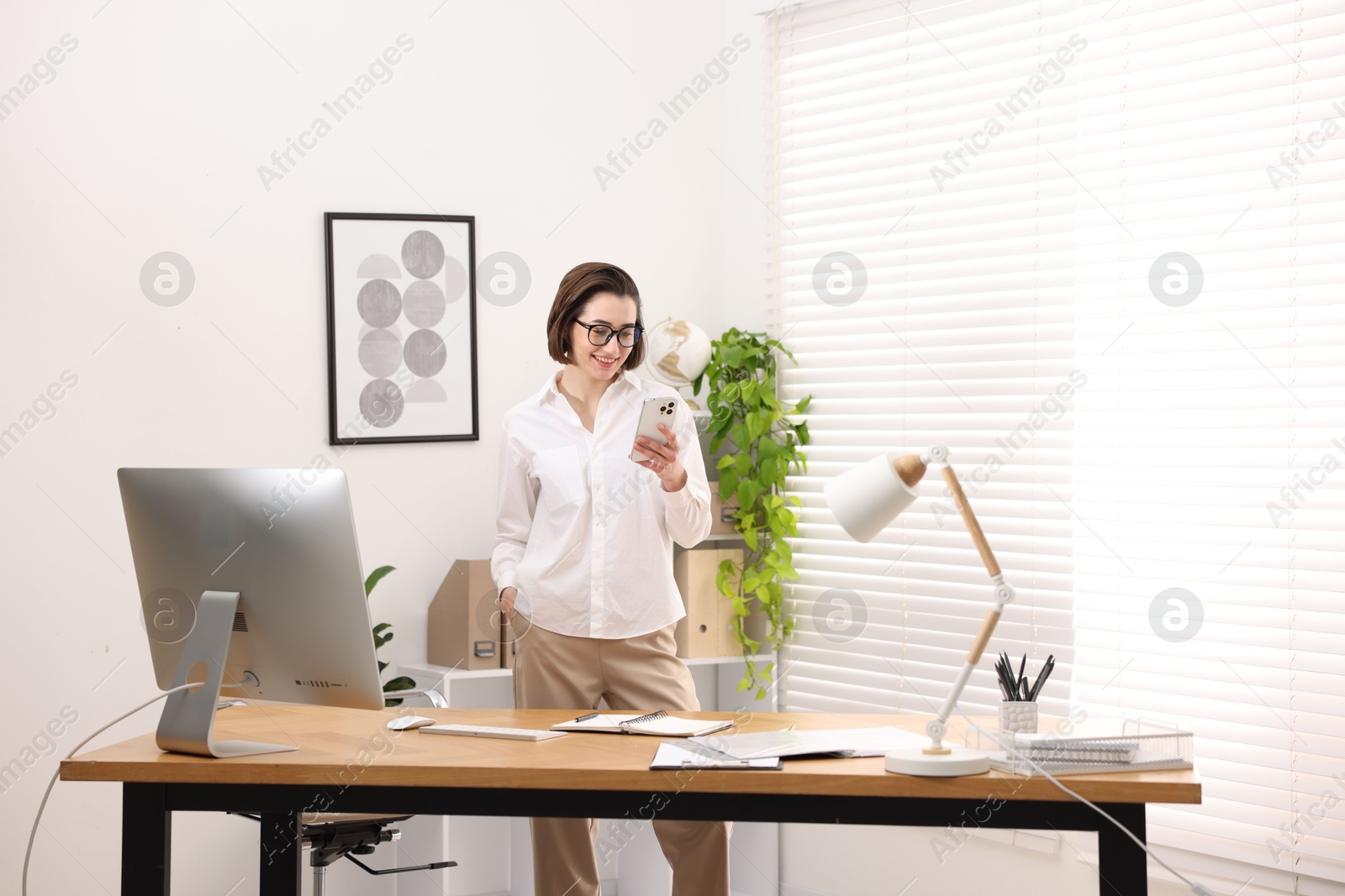 Photo of Smiling secretary with glasses using smartphone in office