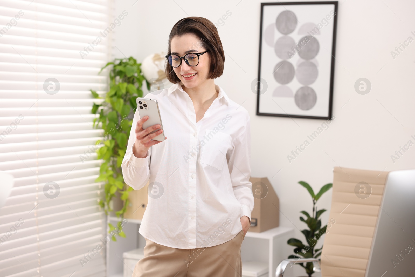 Photo of Smiling secretary with glasses using smartphone in office