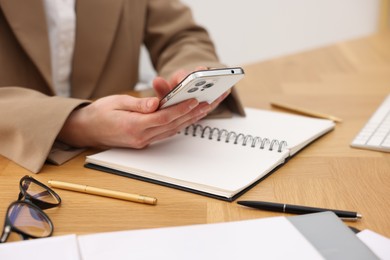 Secretary using smartphone at wooden table in office, closeup