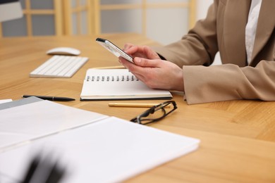 Secretary using smartphone at wooden table in office, closeup