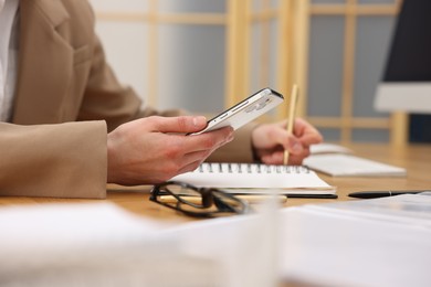 Secretary with smartphone taking notes at table indoors, closeup