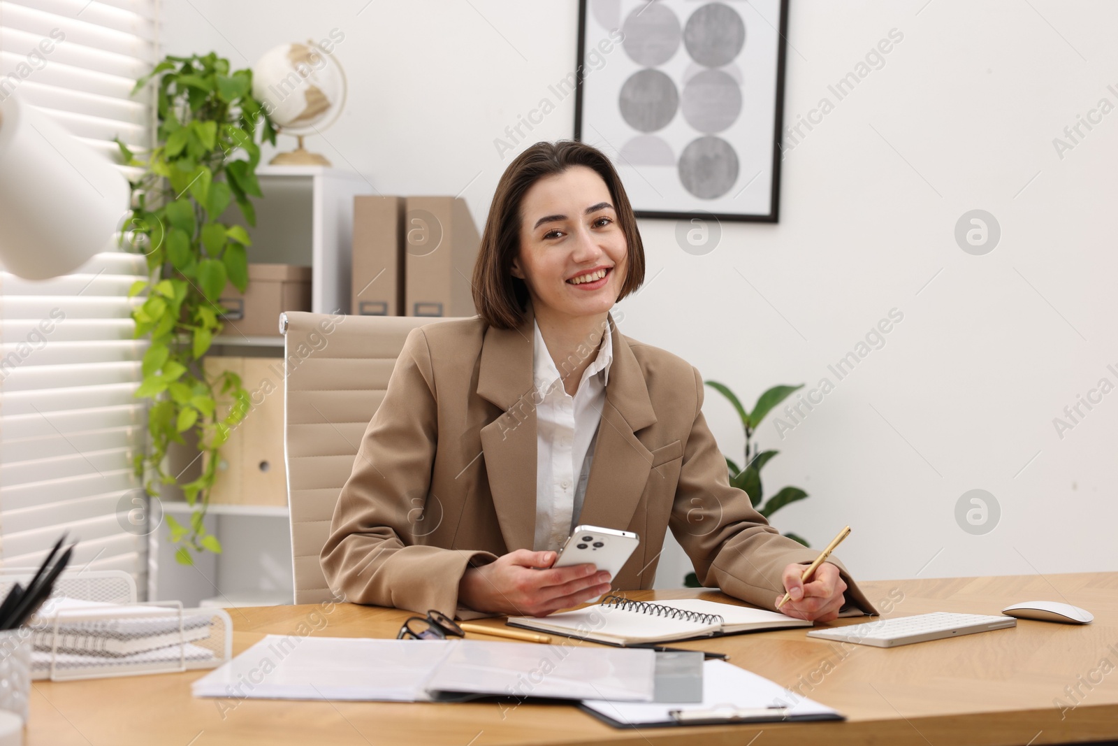 Photo of Secretary with smartphone taking notes at table in office