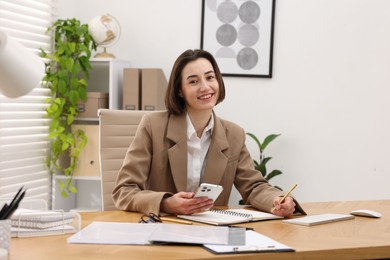 Secretary with smartphone taking notes at table in office