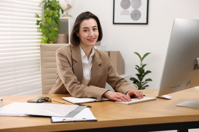 Smiling secretary working on computer at table in office