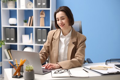 Photo of Smiling secretary working on laptop at table in office