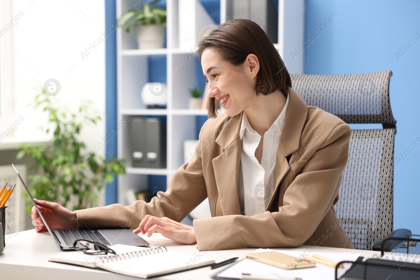 Photo of Smiling secretary working on laptop at table in office