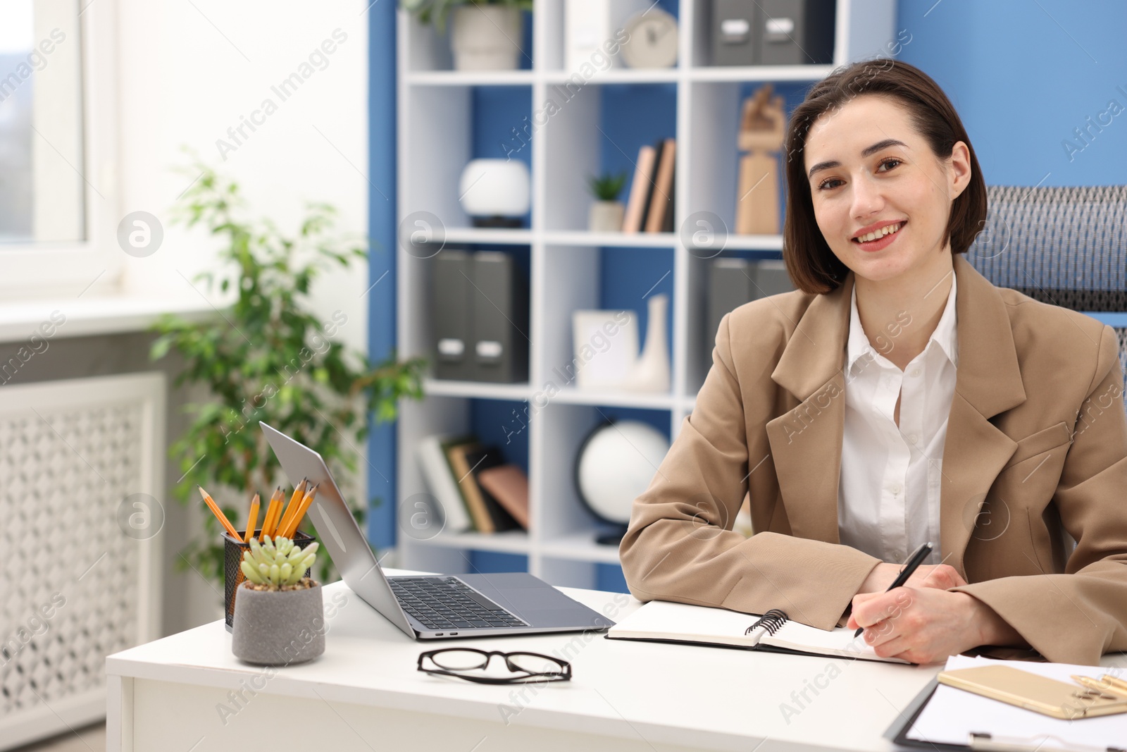 Photo of Smiling secretary taking notes at table in office