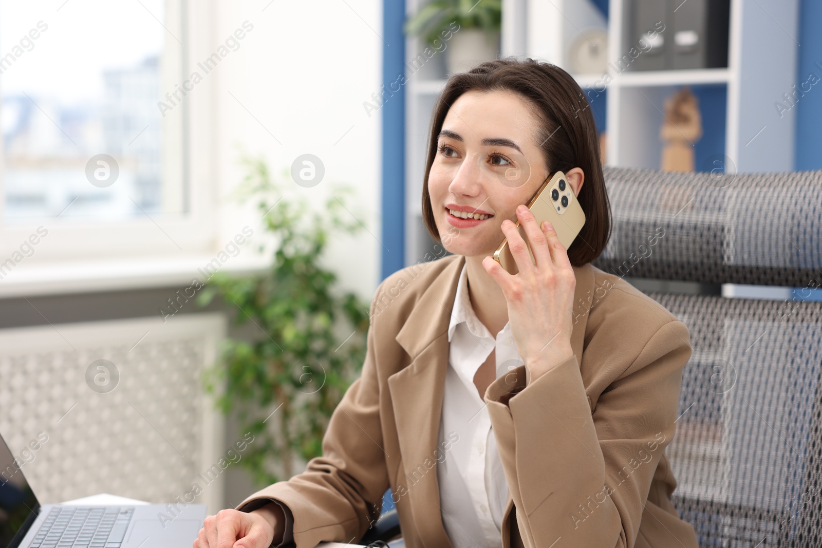 Photo of Secretary talking on smartphone at table in office. Space for text