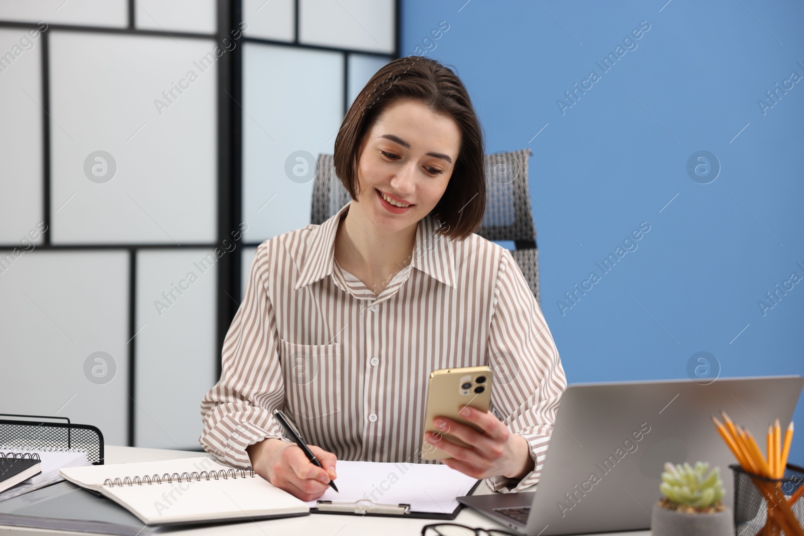 Photo of Smiling secretary using smartphone while working at table in office