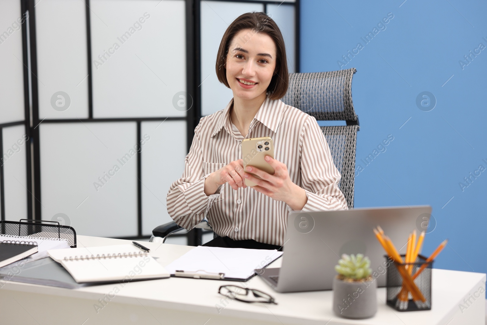 Photo of Smiling secretary using smartphone while working at table in office