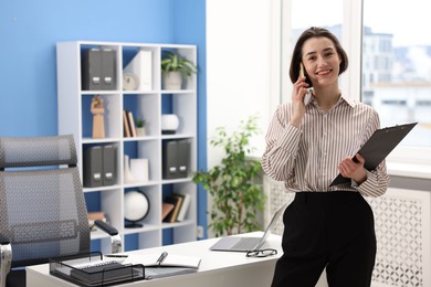 Photo of Smiling secretary talking on smartphone in office