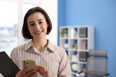 Photo of Smiling secretary with clipboard and smartphone in office. Space for text