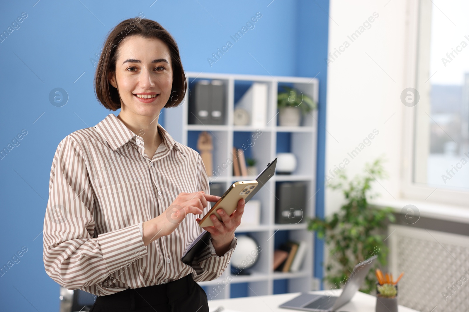 Photo of Smiling secretary with clipboard and smartphone in office. Space for text