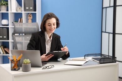 Photo of Smiling secretary taking notes at table in office