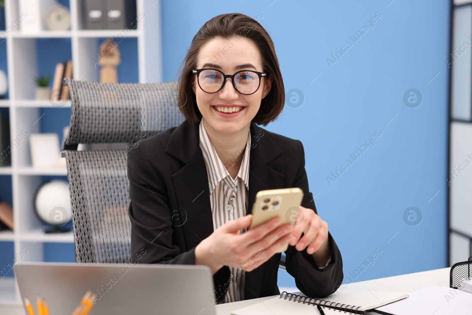 Photo of Secretary with glasses using smartphone at table in office