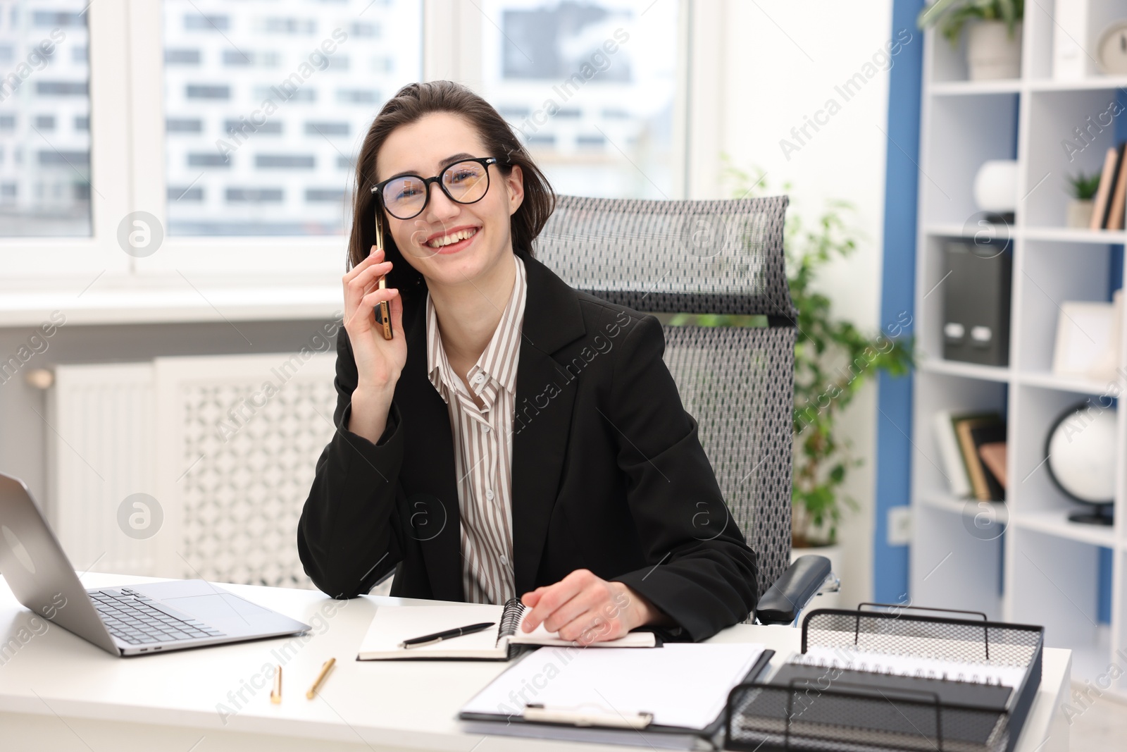 Photo of Smiling secretary talking on smartphone at table in office