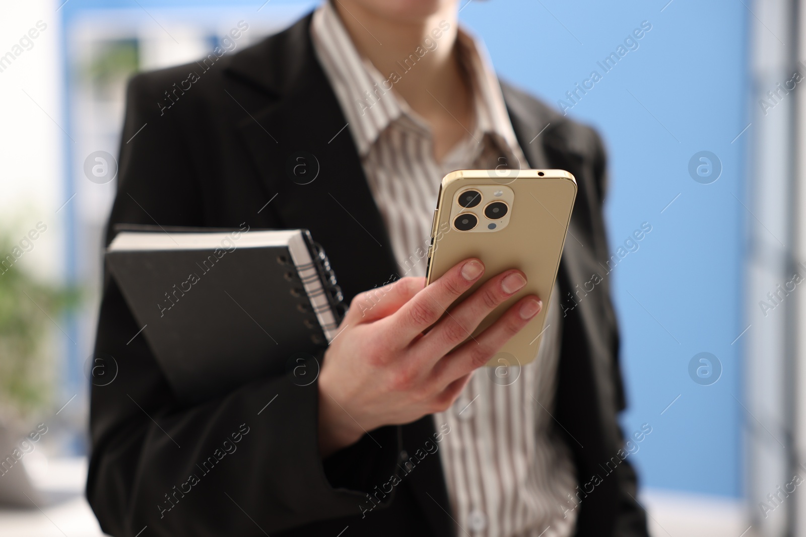 Photo of Secretary with notebook using smartphone in office, closeup