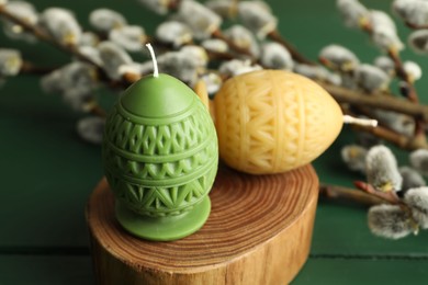 Photo of Colorful egg-shaped candles and willow branches on green table, closeup. Easter decor