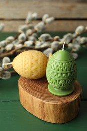 Photo of Colorful egg-shaped candles and willow branches on green wooden table. Easter decor