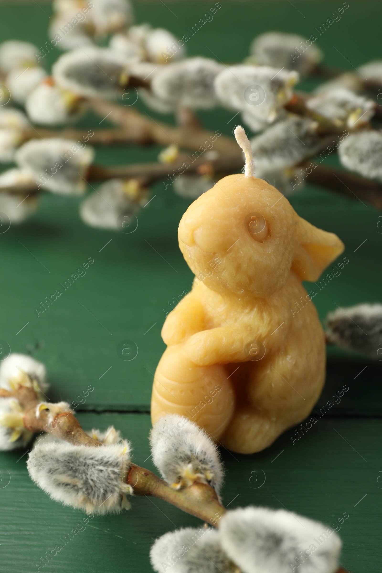 Photo of Yellow bunny-shaped candle and willow branches on green wooden table, closeup. Easter decor