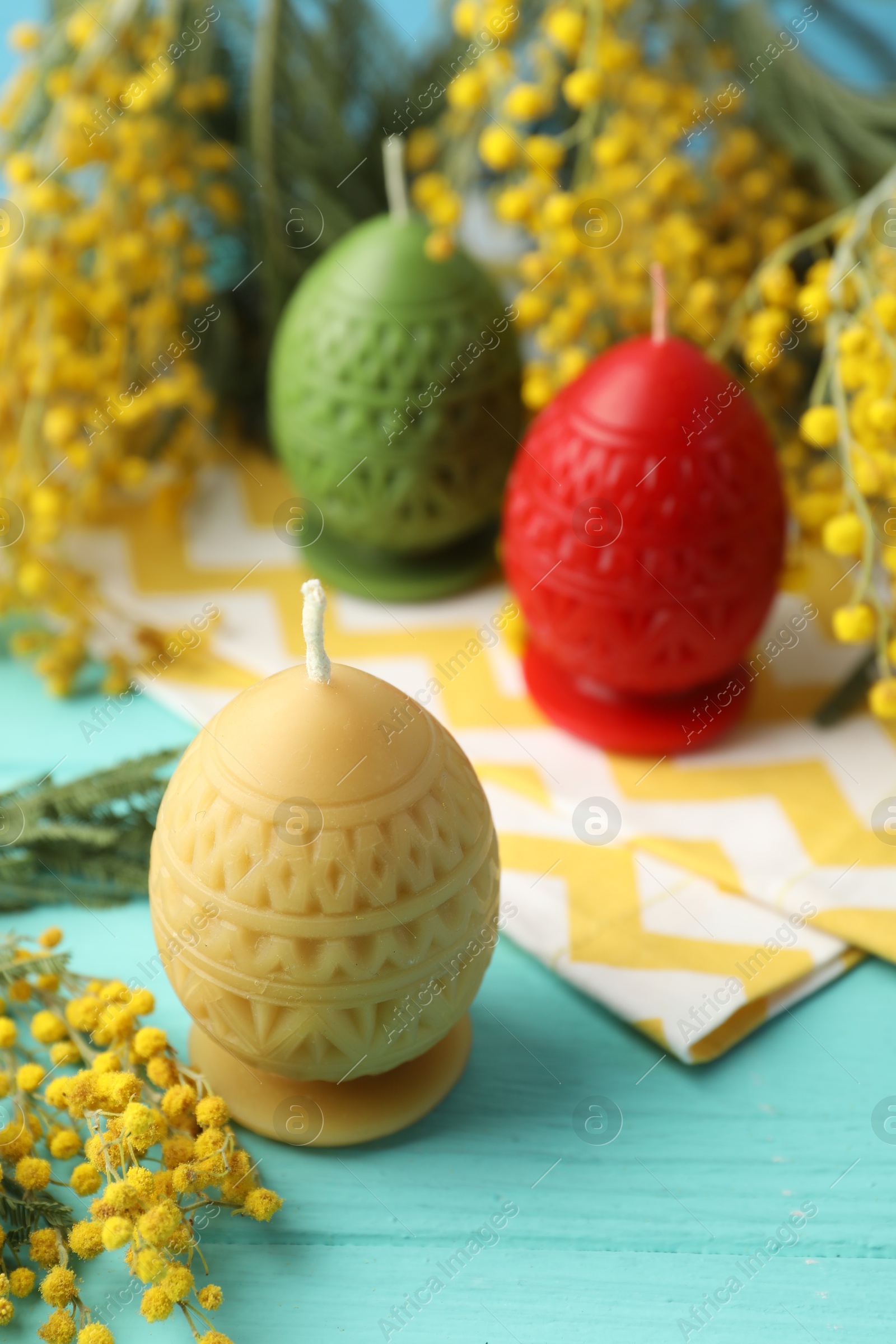 Photo of Colorful egg-shaped candles and mimosa flowers on turquoise wooden table, closeup. Easter decor