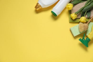 Photo of Spring cleaning. Detergents, supplies and tulips on yellow background, flat lay. Space for text