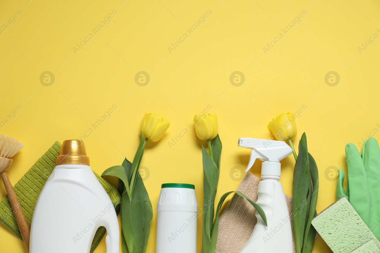 Photo of Spring cleaning. Detergents, supplies and tulips on yellow background, flat lay. Space for text