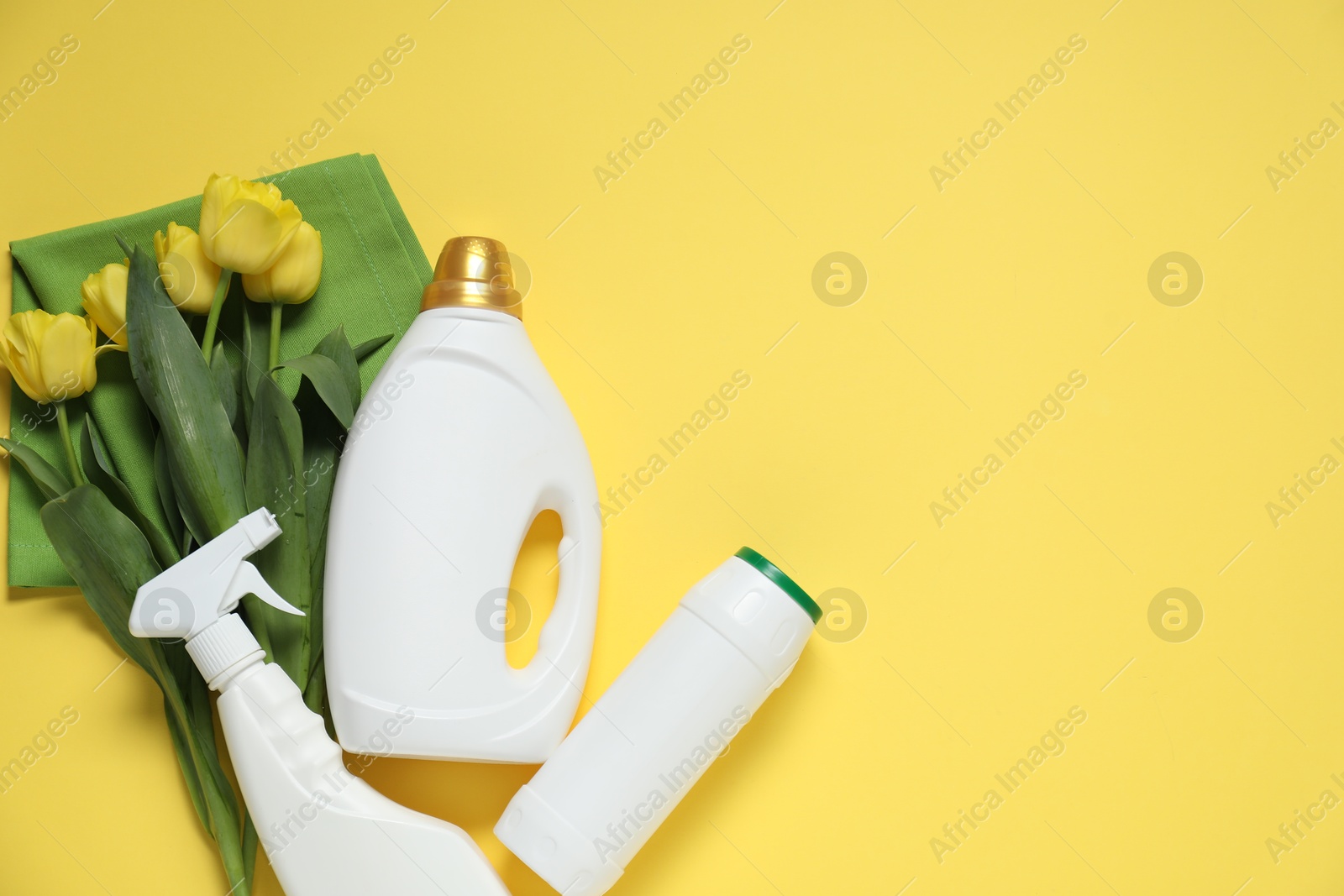 Photo of Spring cleaning. Bottles with detergents, rag and tulips on yellow background, flat lay. Space for text