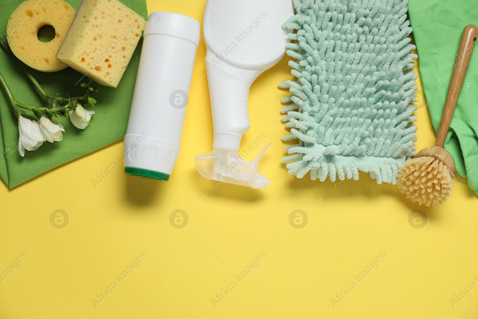 Photo of Spring cleaning. Detergents, supplies and flowers on yellow background, flat lay. Space for text