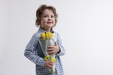 Photo of Cute little boy with bouquet of tulips on white background. Space for text