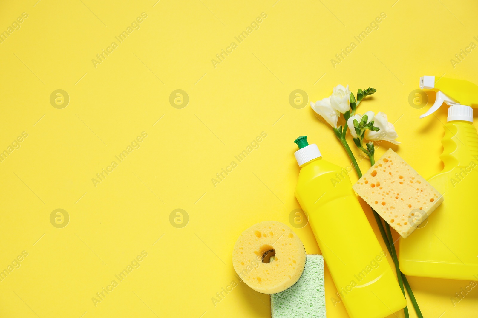 Photo of Spring cleaning. Detergents, sponges and flowers on yellow background, flat lay. Space for text