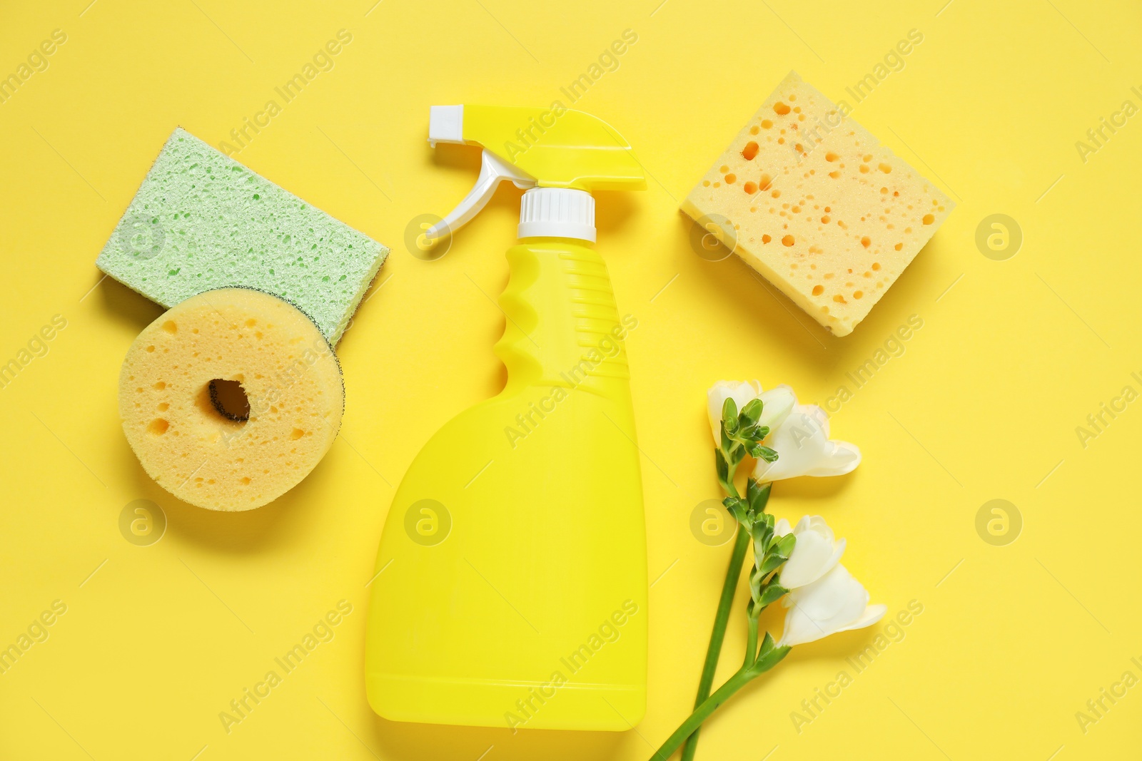 Photo of Spring cleaning. Detergent, sponges and flowers on yellow background, flat lay