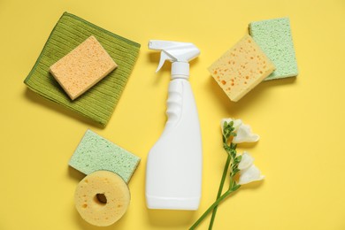 Photo of Spring cleaning. Detergent, supplies and flowers on yellow background, flat lay