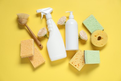 Photo of Spring cleaning. Detergents, supplies and flowers on yellow background, flat lay