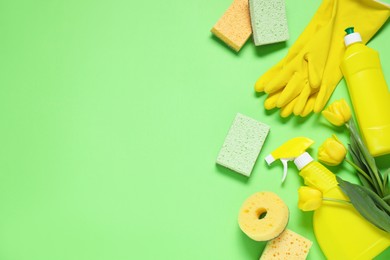 Photo of Spring cleaning. Detergents, supplies and tulips on green background, flat lay. Space for text