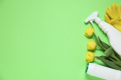 Photo of Spring cleaning. Detergents, gloves and tulips on green background, flat lay. Space for text