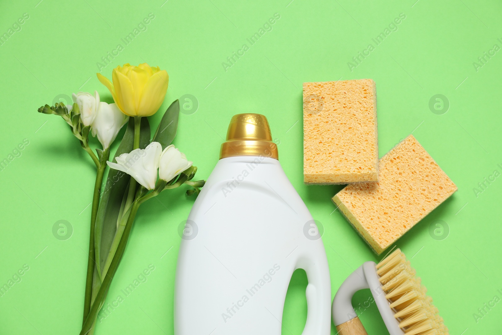 Photo of Spring cleaning. Detergent, supplies and flowers on green background, flat lay