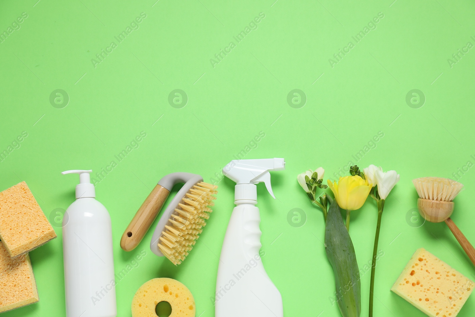 Photo of Spring cleaning. Detergents, supplies and flowers on green background, flat lay. Space for text